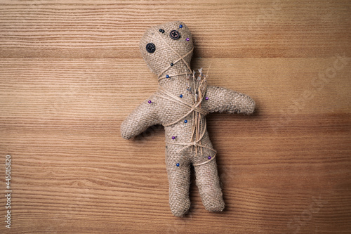 Voodoo doll pierced with pins on wooden table, top view