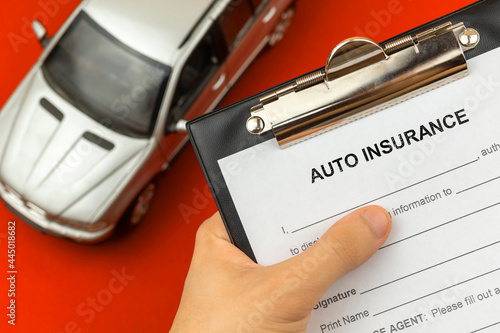 Agent hold Auto and car insurance form in hand. Clipboard with official agreement and policy document. Background with car toy