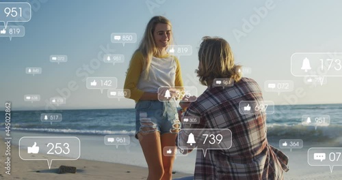 Animation of social media icons over man proposing to his girlfriend on beach