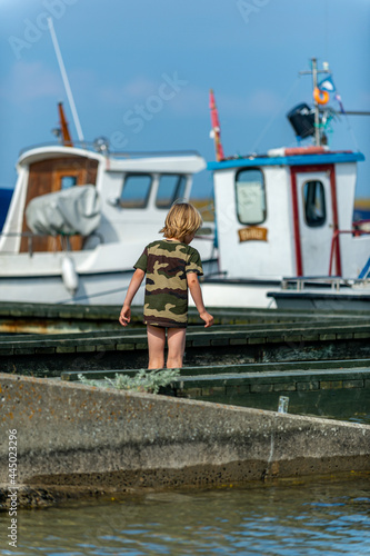 Here army dressed, little boy, watching the water in the marina