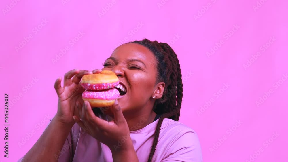 multicultural female holding delicious sweet donut in pink studio background multicultural female holding delicious sweet donut in pink studio background
