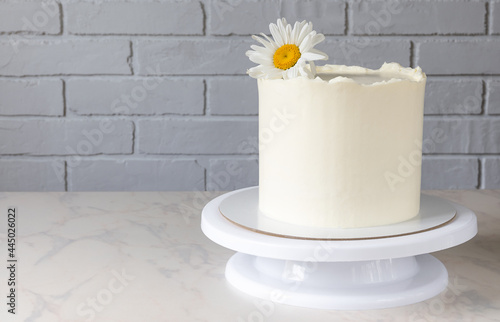 tall white cake on a stand with a decor of a chamomile flower