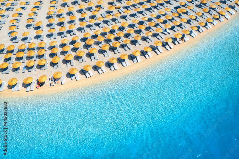 Aerial view of sea, empty sandy beach with sun beds and umbrellas at sunset in summer. Blue lagoon in Oludeniz, Turkey. Tropical landscape with clear turquoise water, deck chair. Travel and nature