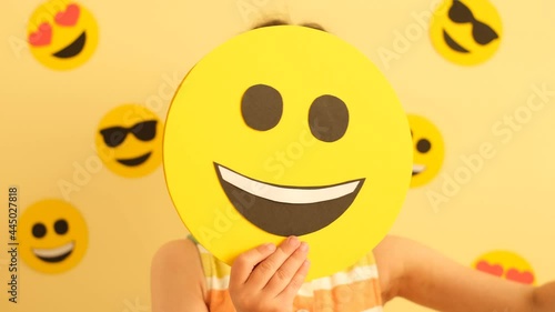 World Smile Day. A little girl with a smiley face changes her emotions. Funny, sad and loving emojis. Anthropomorphic Smiley Face.  photo