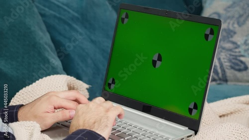 Young man hands typing on keyboard of laptop, chroma green screen of computer. Working and sitting on sofa. Businessman using web camera, remote work at home. photo