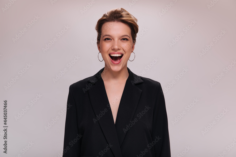 Portrait of brown eyed lady in dark jacket on isolated background. Attractive short-haired woman in black suit laughs and looks into camera on white backdrop Portrait of brown eyed lady in dark jacket on isolated background. Attractive short-haired woman in black suit laughs and looks into camera on white backdrop