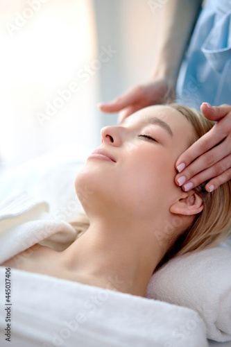 Woman doing relaxing face massage in salon. Hands on temples. Anxiety disappears, tension is relieved. Lady in cozy atmosphere cabin to feel peace and quiet, side view, close-up