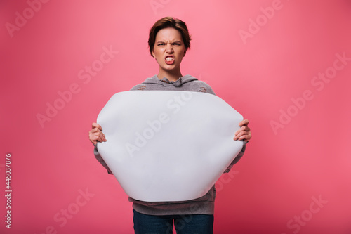 Angry lady looks into camera and holds sheet of paper with place for text. Emotional woman in denim pants looking evil on isolated photo