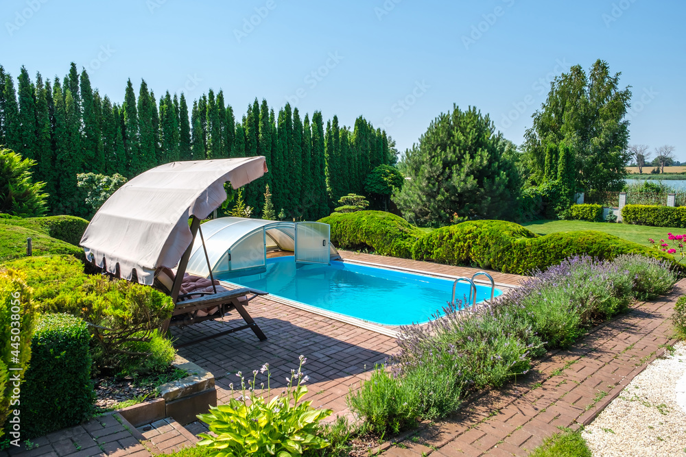 Swimming pool and garden with nicely trimmed bushes and garden swing in backyard