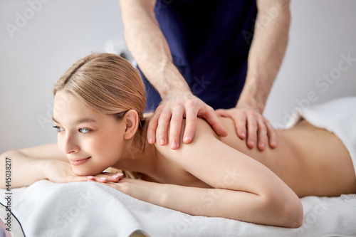Gorgeous lady lying on tummy receiving massage on back by cropped male therapist, caucasian guy in blue uniform carefully massaging back muscles of client. copy space