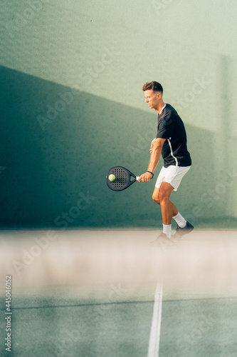 Man playing paddle tennis on an outdoor green paddle tennis court at the sunset
