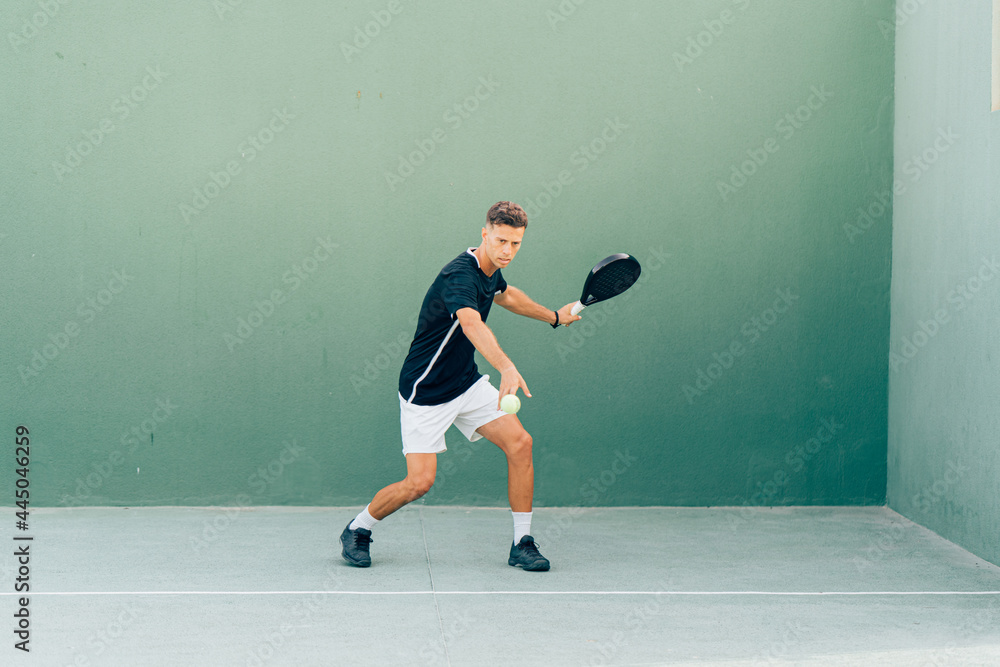 Man playing paddle tennis on an outdoor green paddle tennis court at the sunset