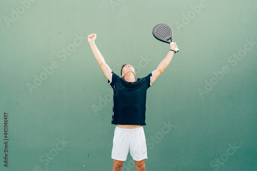 Paddle tennis player celebrating victory at the end of the match on the green court at sunset