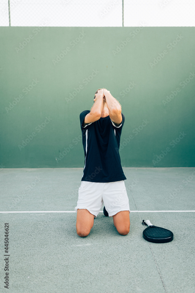 Angry paddle tennis player regretting losing the match on the green court at sunset