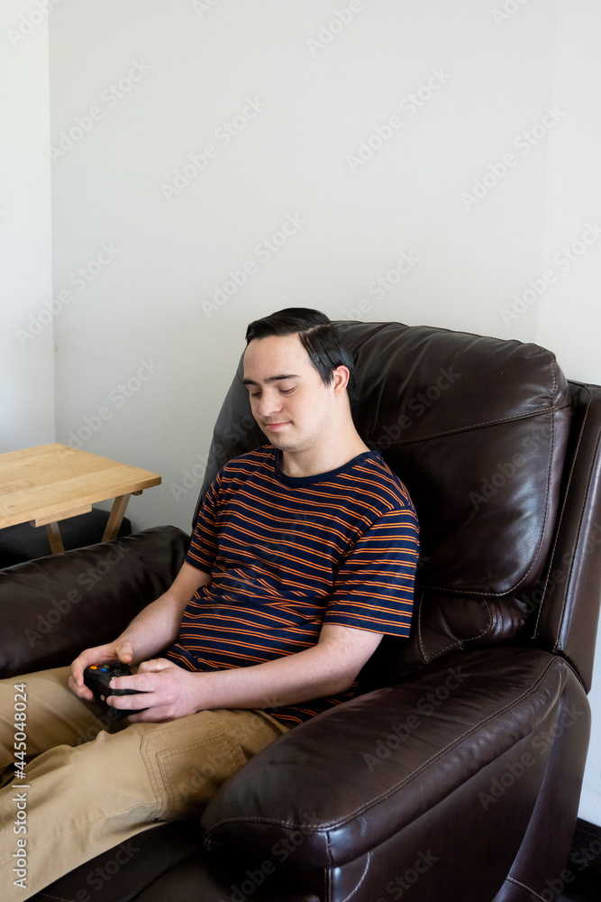 young adult with down syndrome playing video games in couch young adult with down syndrome playing video games in couch