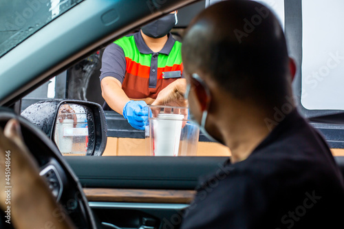 Selective focus to hand of staff wearing medical glove and mask  to handed a food to customer. Drive thru and take away concept.