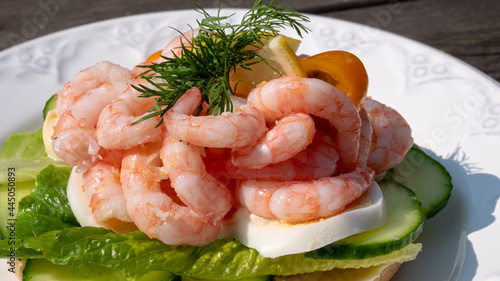 Close up of peeled fresh shrimps on white rye bread, making up a delicious Swedish shrimp sandwich (räkmacka).
Seafood and food preparation concept.