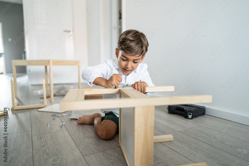 Small caucasian boy four years old playing with self assembly chair or table on the floor at home in day - little child assembling furniture alone childhood craft concept front view copy space Small caucasian boy four years old playing with self assembly chair or table on the floor at home in day - little child assembling furniture alone childhood craft concept front view copy space
