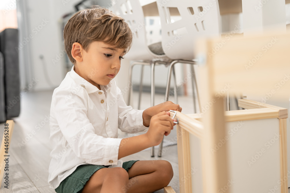 Small caucasian boy four years old playing with self assembly chair or table on the floor at home in day - little child assembling furniture alone childhood craft concept front view copy space Small caucasian boy four years old playing with self assembly chair or table on the floor at home in day - little child assembling furniture alone childhood craft concept front view copy space