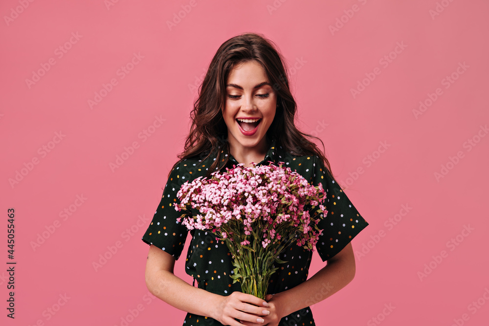 Happy woman in polka dot outfit holds bouquet on pink background. Charming excited girl posing with beautiful pink flowers on isolated Happy woman in polka dot outfit holds bouquet on pink background. Charming excited girl posing with beautiful pink flowers on isolated