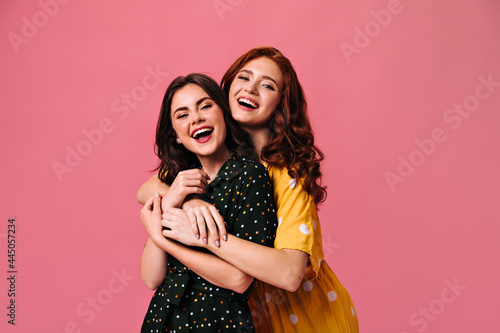 Charming ladies look into camera and hug. Fashionable women in great polka dot dresses have fun together and embrace photo