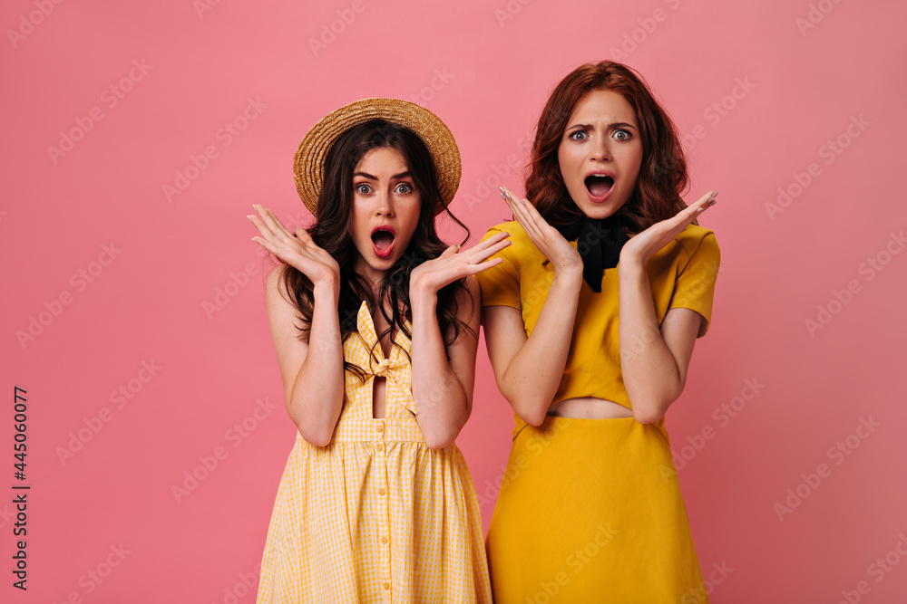 Surprised girls in yellow outfits posing on pink background. Young beautiful women in summer dresses are surprised on isolated background Surprised girls in yellow outfits posing on pink background. Young beautiful women in summer dresses are surprised on isolated background