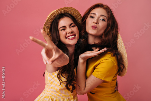 Portrait of happy girls in yellow outfits on pink background. Amazing young women with curly hair in good mood have fun and smile