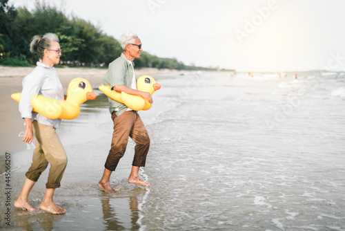 Senior couple take off and throw the face mask while happily running down to the beach. Senior couple show hands with enjoying on the beach, plan life insurance and retirement concept..
