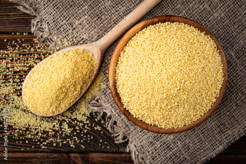 Quadro su tela Dry couscous in wooden bowl on dark wooden background.