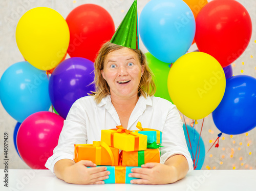 Woman hugging many gifts in a festive cap on a background of colorful balloons