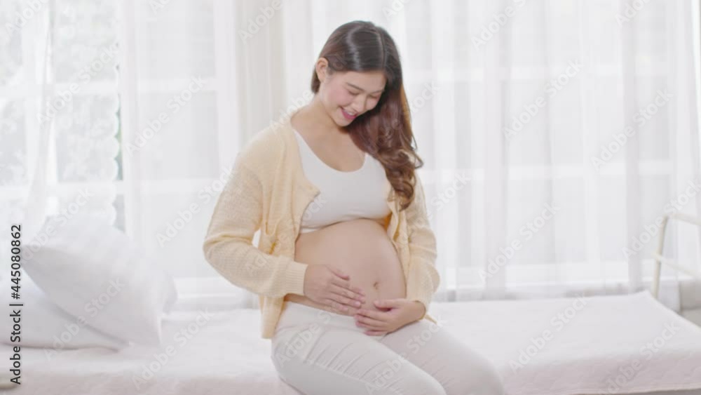 Happy Pregnant Woman sitting on bed holding and stroking her big belly at home,Pregnancy of young woman enjoying with future life relax at home,Motherhood and Pregnant Concept Happy Pregnant Woman sitting on bed holding and stroking her big belly at home,Pregnancy of young woman enjoying with future life relax at home,Motherhood and Pregnant Concept