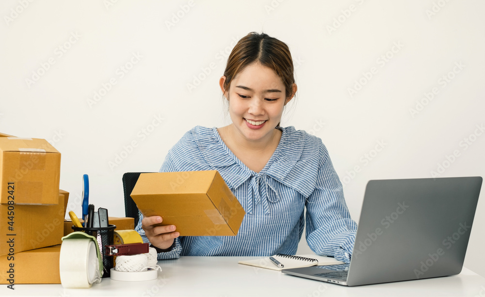 Young Asian woman business owner with many parcel boxes on the table happy online sales job, use the laptop, get an order from customers, take notes, and make arrangements for delivery by post Young Asian woman business owner with many parcel boxes on the table happy online sales job, use the laptop, get an order from customers, take notes, and make arrangements for delivery by post