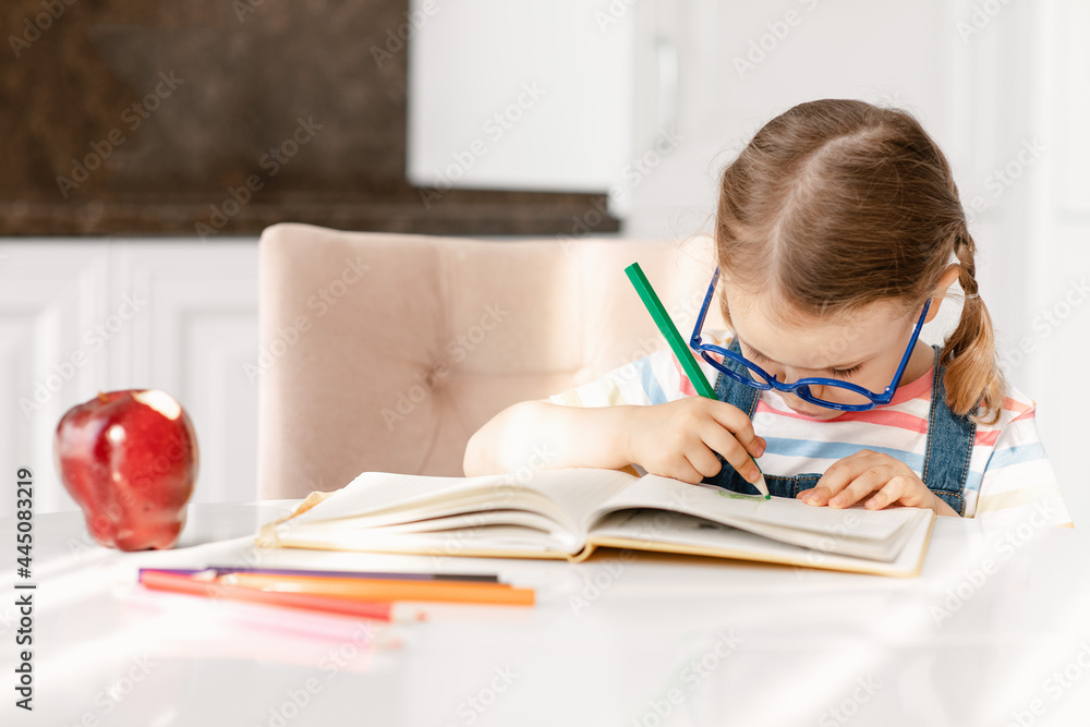 Smart child girl with glasses draws colored pencils at table in white kitchen. Developing children's skills, kid hobbies, education and learning, back to school. Background, copy space Smart child girl with glasses draws colored pencils at table in white kitchen. Developing children's skills, kid hobbies, education and learning, back to school. Background, copy space
