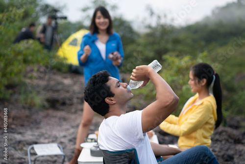 young man drinking water while camping with friends. adventure camping concept