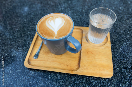 Hot of Latte coffee with heart pattern and cold water glass in a cup on wooden tray on marble table