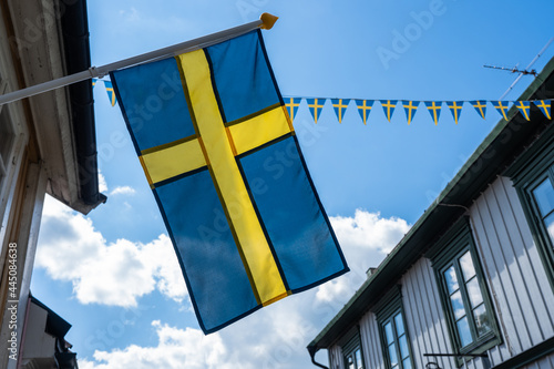 Beautiful small Swedish flag is hung on the house wall. Decoration of houses and streets with flags. National holiday. Day of Sweden. Pennants hanging from rope between the houses outside.