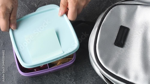 Women hands puts in lunch box with a sandwich, cookies and cherries from a backpack. Concept of a snack at school, office, outside the home.