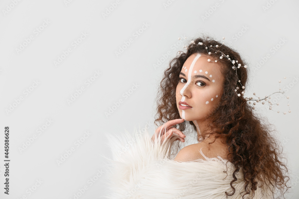 Beautiful young African-American woman with paint on her face against light background