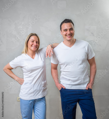 two people, team of physiotherapists, smiling colleagues portrait. standing in front of a gray wall.