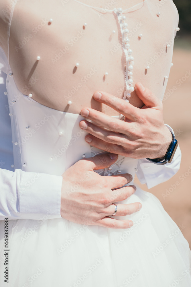 Obraz premium The groom hugs the bride. Vertical photo of the bride and groom. Beautiful buttons on the bride's back. Gentle hugs of the newlyweds