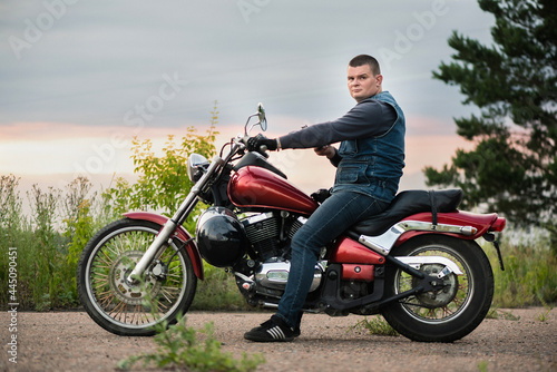 A motorbiker is sitting on the motorbike with a mobile phone in his hand.