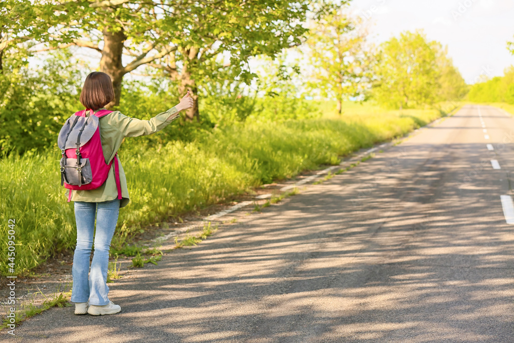 Young woman with backpack hitchhiking on road Young woman with backpack hitchhiking on road