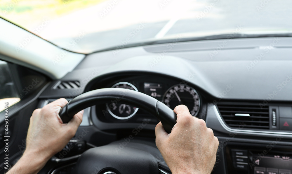 Male hands on the steering wheel of a car, inside view. Vehicle management, close-up view of the dashboard and interior. The man behind the wheel.