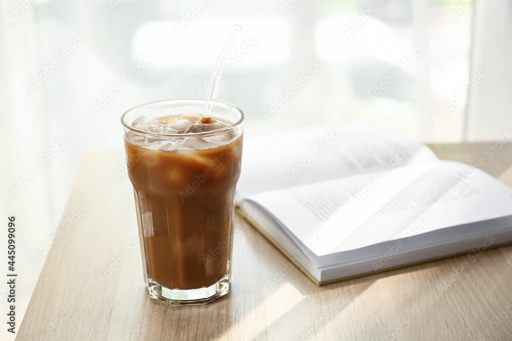 Glass of tasty ice coffee with milk and book on wooden table Glass of tasty ice coffee with milk and book on wooden table