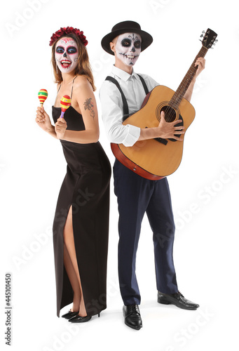 Young couple with painted skull on faces, maracas and guitar against white background. Celebration of Mexico's Day of the Dead (El Dia de Muertos)