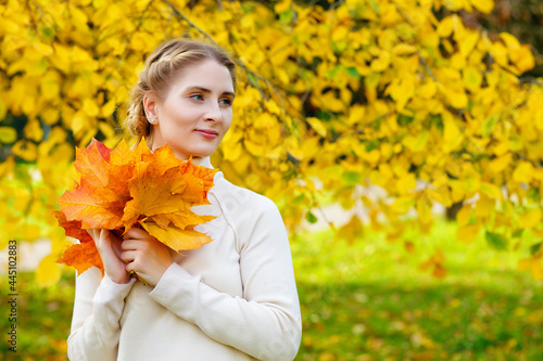 Woman in an autumn park. An emotional portrait of a cute and positive beautiful blonde girl with a bouquet of maple leaves on a background of blurred yellow foliage