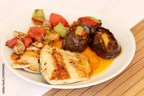 Fish and vegetables are served on a white plate on a wooden table. Healthy food, grilled trout with tomatoes, peppers and eggplant