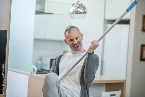 Man in homewear holding a mop and playing an air guitar photo