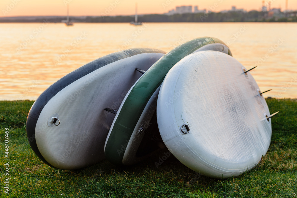 Obraz premium Three SUP boards lying on the grass by the river, lake or sea.