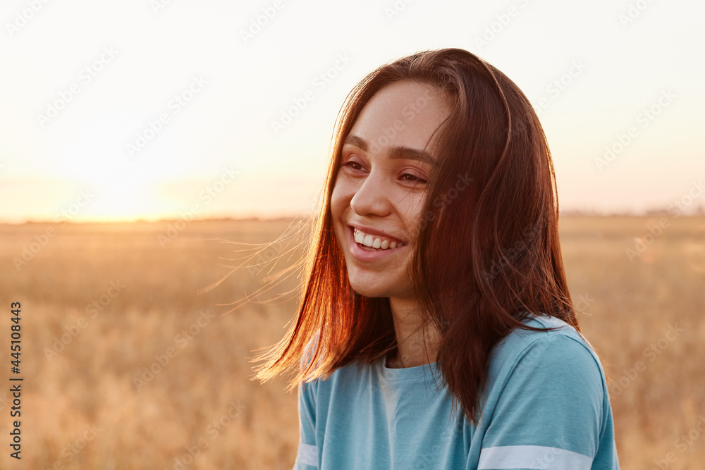 Fototapeta premium Summer portrait of laughing happy woman outdoor, enjoying warm sunshine, wearing blue t shirt, having dark hair, looking away with toothy smile, expressing happiness.